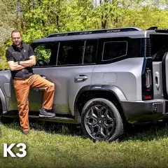 Uomo appoggiato al nuovo SUV grigio, un Ickx K3, in un prato verde.
