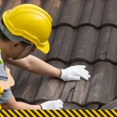 Budowlaniec w żółtym kasku naprawia dachówkę. Potrzebny jest mocny klej do dachówek, by wszystko trzymało się jak należy.