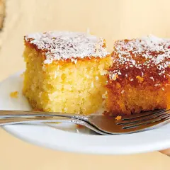 Två saftiga bitar kokos kaka, toppade med riven kokos, ligger på en vit tallrik med två gafflar.