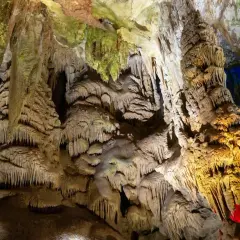 Wnętrze jaskini Prometeusza, pełne stalaktytów i stalagmitów, oświetlone ciepłym, żółtym światłem i niebieskimi akcentami.