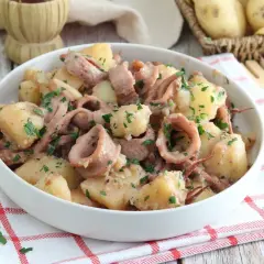 Un saporito piatto di totani e patate, condito con prezzemolo fresco, servito in una ciotola bianca su un tovagliolo a quadri rossi.