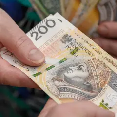 Dwie dłonie przekazują sobie banknot 200 zł. Czy wychowanie dzieci liczy się do emerytury?