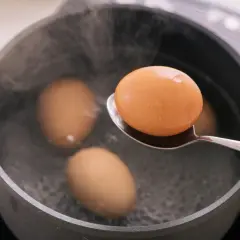 Une cuillère sort un œuf à la coque de l'eau bouillante. Trois autres œufs sont dans la casserole.