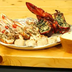 En tallrik med grillade skaldjur, inklusive hummer och havskräftor, serveras med en skål dippsås.