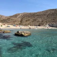 Aguas cristalinas en la cala del medio, con gente disfrutando del sol y el mar en un día soleado.