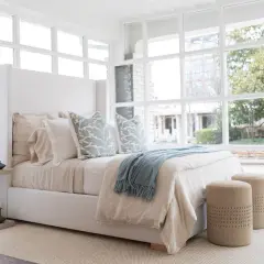 A light blue throw with fringe adds a cozy touch to this serene bedroom, draped over a bed with linen bedding.