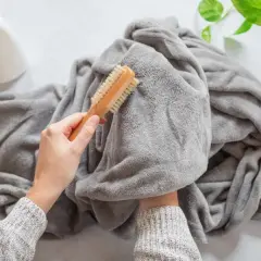 A person is brushing a grey throw blanket, showing how to wash it. A spray bottle is nearby.