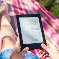 Une personne lit un livre électronique sur un écran e-ink, confortablement installée dans un hamac.