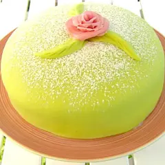 En vacker prinsesstårta med grön marsipan, pudrad med florsocker och dekorerad med en rosa ros och gröna blad. Perfekt för ett prinsesstårta recept!