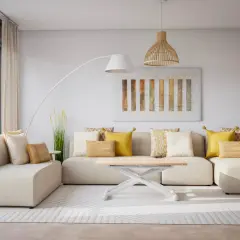 Sofá modular beige con cojines amarillos y blancos, mesa de centro blanca, lámpara de pie y cuadro abstracto. Un espacio acogedor sin ruido visual.