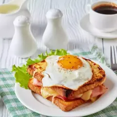Un délicieux croque monsieur garni d'un œuf au plat, servi avec une tasse de café et une sauce crémeuse.