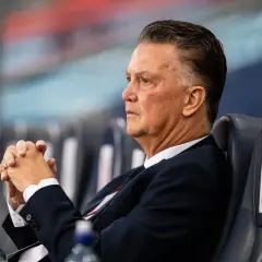 Louis van Gaal, znany z prowadzenia drużyny z pasją, siedzi z zamyślonym wyrazem twarzy, dłonie splecione.