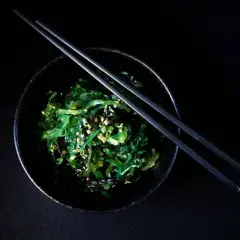 Insalata di wakame, un piatto ricco di **wakame proprietà** benefiche, guarnita con semi di sesamo e cipollotto, pronta per essere gustata con le bacchette.