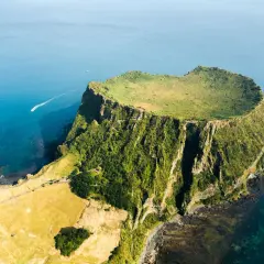 Un cratere vulcanico verdeggiante, tra le meraviglie naturali del mondo, si erge dal mare blu. Una barca solca le acque.