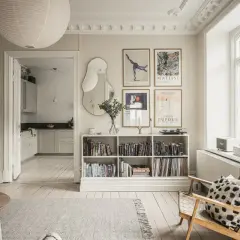 Salón con estilo de Estocolmo: estanterías blancas llenas de libros, arte en las paredes, silla de madera y alfombra gris.