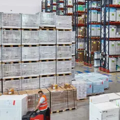 Pracownik obsługuje wózek widłowy w magazynie, gdzie panuje **skladowanie blokowe** towarów w dużych skrzyniach i na paletach.