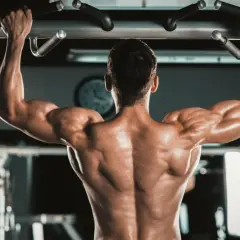 Mężczyzna wykonuje podciąganie na drążku, napinając potężne **biceps**y.