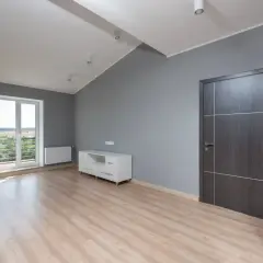 Nowe mieszkanie TBS z jasnym drewnianym parkietem, szarymi ścianami, drzwiami i białym meblem RTV.