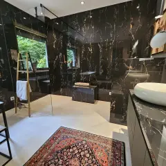 Luxuriöses Bad ohne Fenster mit schwarzem Marmor, freistehender Badewanne, Dusche und Waschbecken. Ein bunter Teppich liegt auf dem Boden.