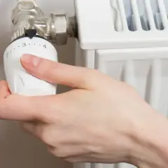 Mano girando la perilla del radiador hacia la izquierda para cerrarlo.