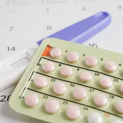 Test ciążowy i blister tabletek antykoncepcyjnych na tle kalendarza. Decyzje o płodności, planowanie rodziny, vixpo.