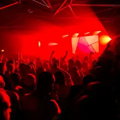 Folla in delirio in una discoteca di Parigi per giovani, illuminata da luci rosse e un palco geometrico.