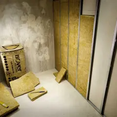 Isolering av glasull, som kan vara farligt att hantera, ligger utspritt. En rulle Isover står mot en rå betongvägg.