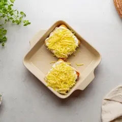 Dwa tosty z szynką i serem, przygotowane do zapieczenia, jak w klasycznym croque madame. Obok gałka muszkatołowa i świeża zielenina.