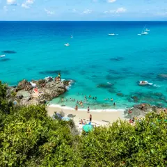 Spiaggia con acque cristalline e gente che nuota e prende il sole. Un luogo ideale per il tuo prossimo viaggio in Calabria mare dove andare.