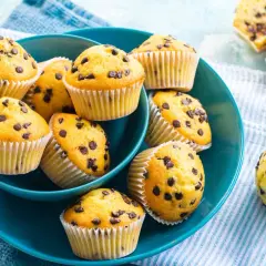 Muffin con gocce di cioccolato, dorati e invitanti, serviti in una ciotola blu. Perfetti per una pausa golosa.