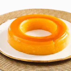 Un delicioso tocino de cielo, con su característico color dorado y forma de anillo, reposa sobre un plato blanco con borde dorado.