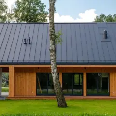 Nowoczesny dom szkieletowy bez pozwolenia, z drewnianą elewacją i szarym dachem, otoczony zielenią.