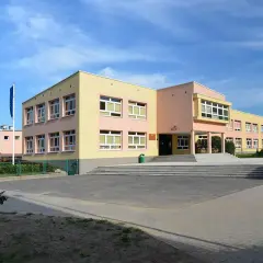 Kolorowy budynek szkoły z flagami przed wejściem. To miejsce, gdzie kiedy powstalo gimnazjum, uczniowie zdobywali wiedzę.