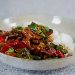 En skål med ris och en smakrik kyckling cashew-röra med paprika, champinjoner och salladslök.