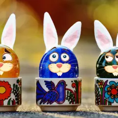 Trzy pisanki z króliczymi uszami w ozdobnych kieliszkach. Zastanawiają się, ile trwa Wielkanoc w Niemczech.