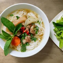 Aromaticzny makaron pho z kawałkami mięsa, warzywami i świeżymi ziołami. Obok talerz z sałatą i kiełkami fasoli.