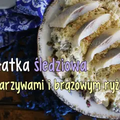 Sałatka śledziowa z warzywami i brązowym ryżem, ozdobiona kawałkami marynowanych śledzi.