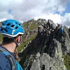 Alpinista w niebieskim kasku patrzy na grań Tatr, gdzie wspina się grupa ludzi.