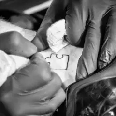 Ręce w rękawiczkach tworzą tatuaż puzzle, symbol autyzmu.