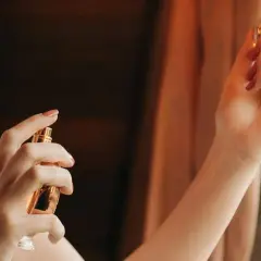 Dłoń trzymająca złoty flakonik perfum, z pierścionkiem na palcu.