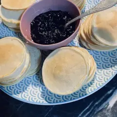 Une assiette bleue et blanche présente des piles de poffertjes dorés, accompagnés d'un bol de confiture de myrtilles. Parfait pour une recette de poffertjes !