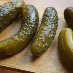 Kilka ogórków kiszonych leżących na drewnianej desce.