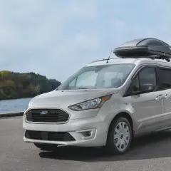 Silver Ford Transit Connect med takbox vid en sjö. Inga problem här, bara en redo för äventyr.