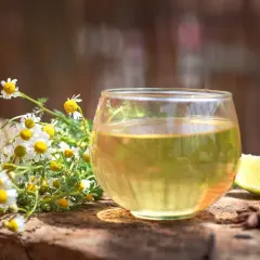 Jak zaparzyć rumianek? Świeże kwiaty rumianku, szklanka naparu, plasterek limonki i anyż na drewnianym blacie.