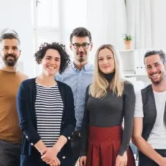 Fünf lächelnde Personen stehen im Büro. Sie haben erfolgreich ihr Fernstudium anerkannt und feiern ihren Erfolg.