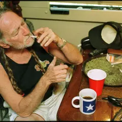 Willie Nelson, icona delle canzoni country famose, si accende una sigaretta con una tazza di caffè accanto.