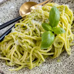 Cremige Avocado-Pasta mit frischem Basilikum und Parmesan auf einem rustikalen Teller, serviert mit schwarzem Besteck.