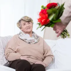 Uśmiechnięta starsza pani otrzymuje bukiet czerwonych róż. To piękny gest z okazji 60 rocznicy ślubu.