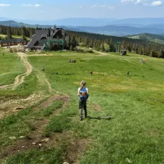 Dziecko z plecakiem idzie ścieżką na hali miziowej. W oddali budynki i góry.