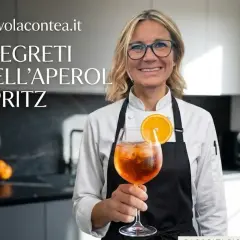 Donna sorridente con un bicchiere di Aperol Spritz, decorato con una fetta d'arancia. La scritta "I segreti dell'Aperol Spritz" è visibile.
